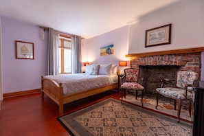 A bedroom with a wooden bed, a fireplace, two chairs, and a rug. - Le Foyer d'Antan (3-1116) (Québec City)