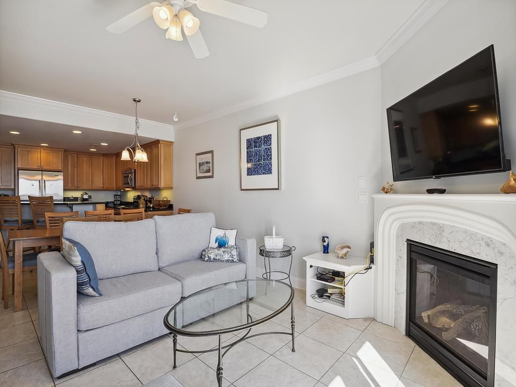 A living room with a sofa, coffee table, fireplace, TV, and kitchen in the background.