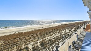 En strand med utsikt över en strandpromenad, havet och sanddyner.