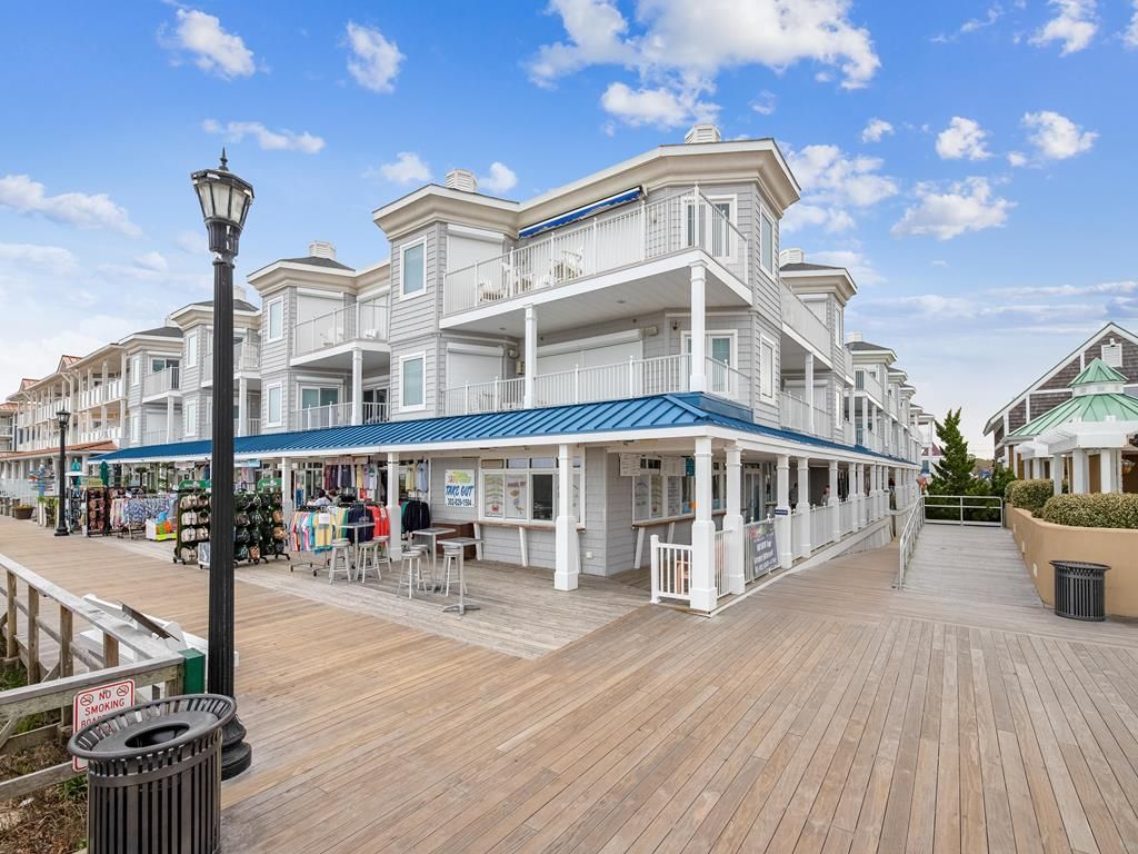 A waterfront boardwalk with a row of white buildings, a no smoking sign, and outdoor seating areas.