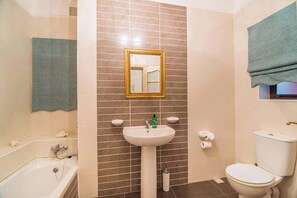 Une salle de bain équipée d’une baignoire, d’un lavabo, d’un miroir, de toilettes et d’un porte-serviettes.