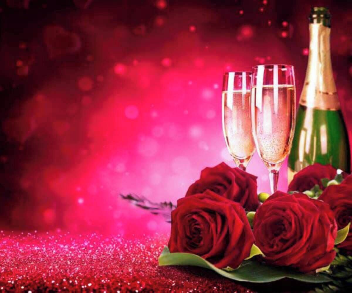 A table with two champagne flutes, a bottle, and several red roses.