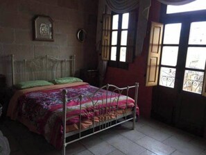 Une chambre à coucher avec un lit en métal, une couvre-lit à motifs et une fenêtre donnant sur un paysage agréable.