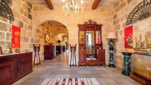 Un pasillo amplio con paredes de piedra, un candelabro y muebles antiguos.