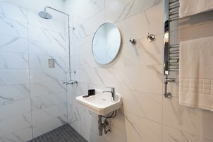 A modern bathroom with a marble-tiled wall, a round mirror, a sink, and a towel rack.