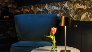 Una stanza con una sedia blu, un tavolino rotondo con una lampada e un vaso con un'unica tulipano.