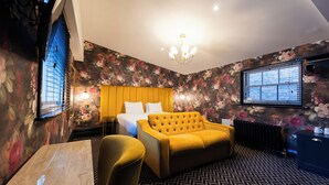 Una camera d'albergo con un letto, un divano giallo, un tavolo da pranzo e un lampadario.