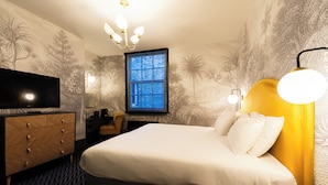 Una camera d'albergo con un letto grande, una televisione, un comò e una finestra con persiane.