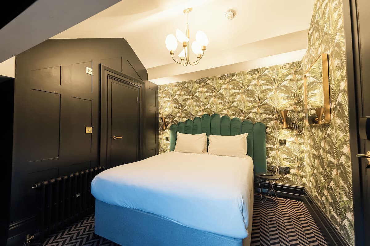 Una camera d'hotel con un letto grande, una testiera imbottita verde, carta da parati decorata e un lampadario.