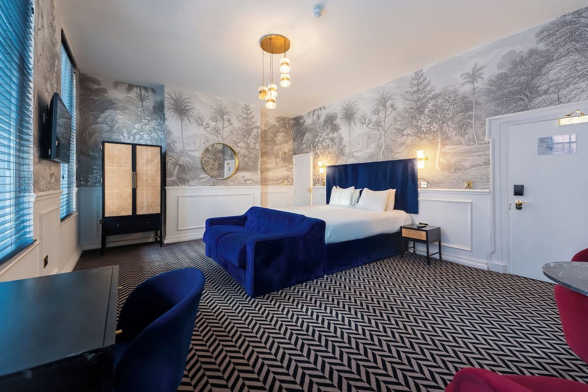 Una camera d'hotel con un letto, una scrivania, una sedia, un armadio e una parete decorata con un murale tropicale.