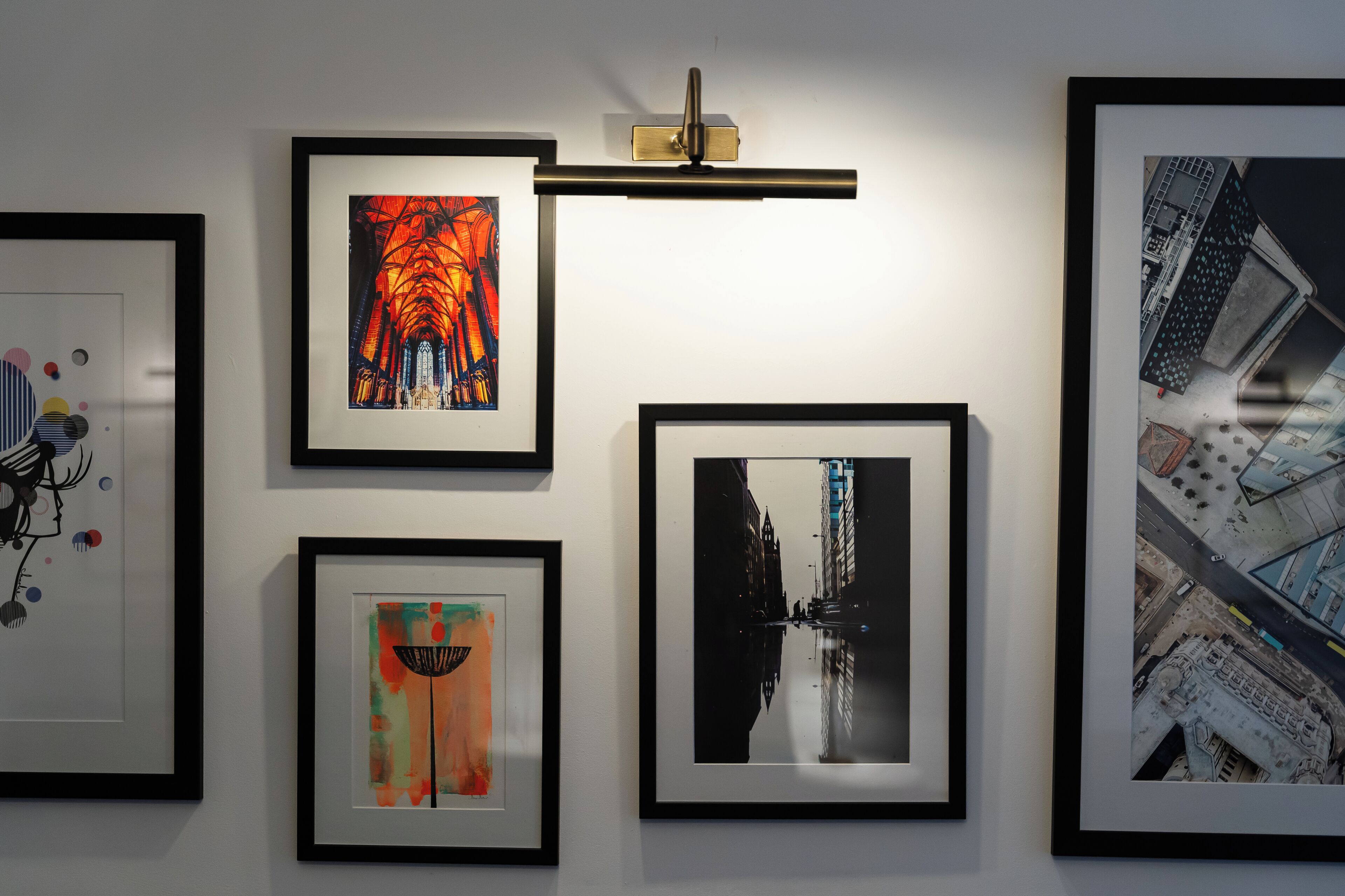 Una pared de galería con obras enmarcadas, incluyendo una vista urbana y piezas abstractas.