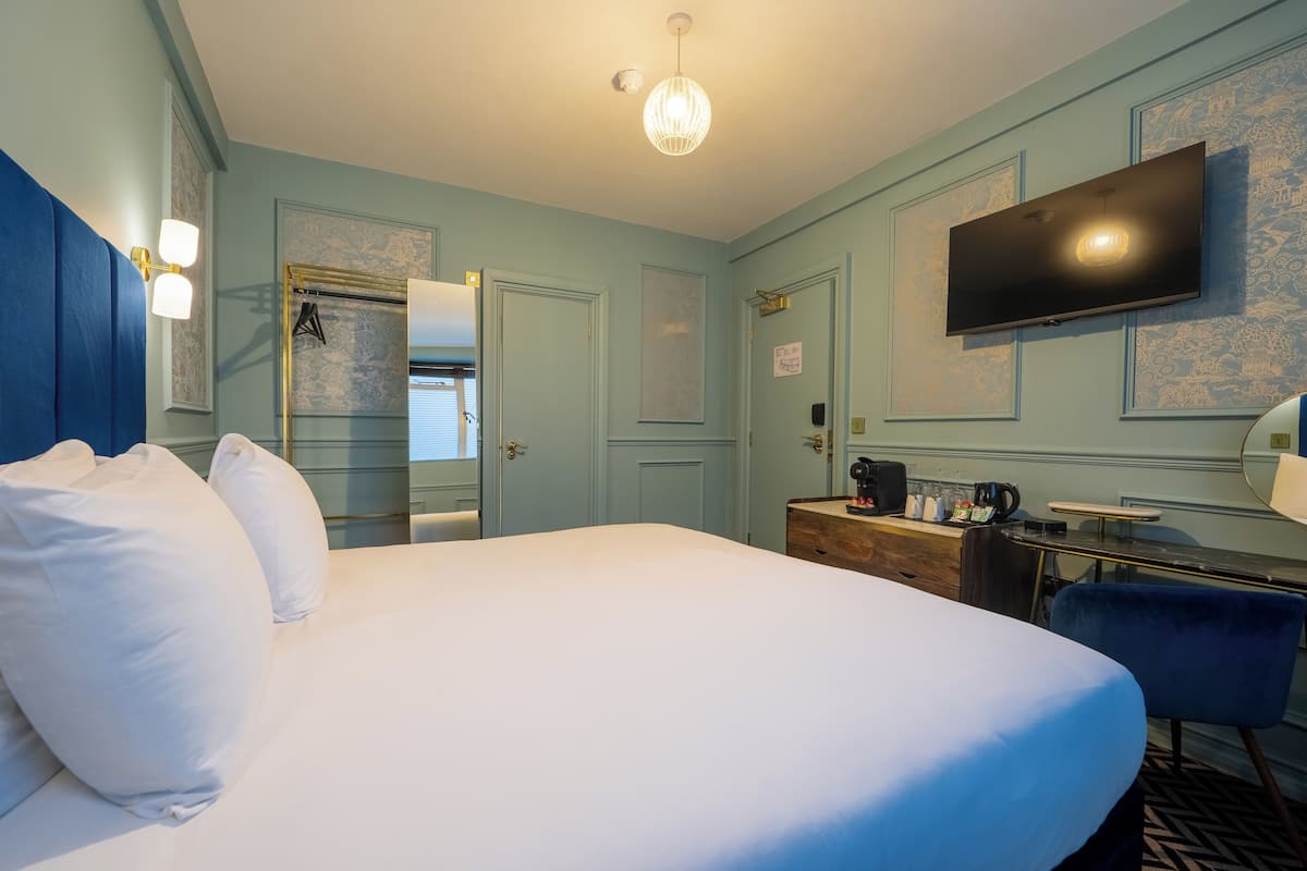 Camera d'albergo con un letto grande, una scrivania con una macchina per caffè, una TV a schermo piatto e un armadio.