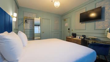 A hotel room with a large bed, a desk with a coffee maker, a flat-screen TV, and a wardrobe.