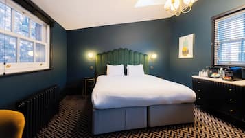 A modern bedroom with a large bed, a chest of drawers, a vanity, and a window with blinds.