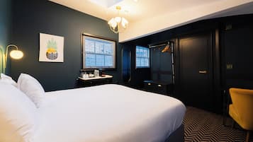 Une chambre d’hôtel avec un grand lit, un bureau avec une lampe, une chaise, une armoire et une fenêtre avec des stores.