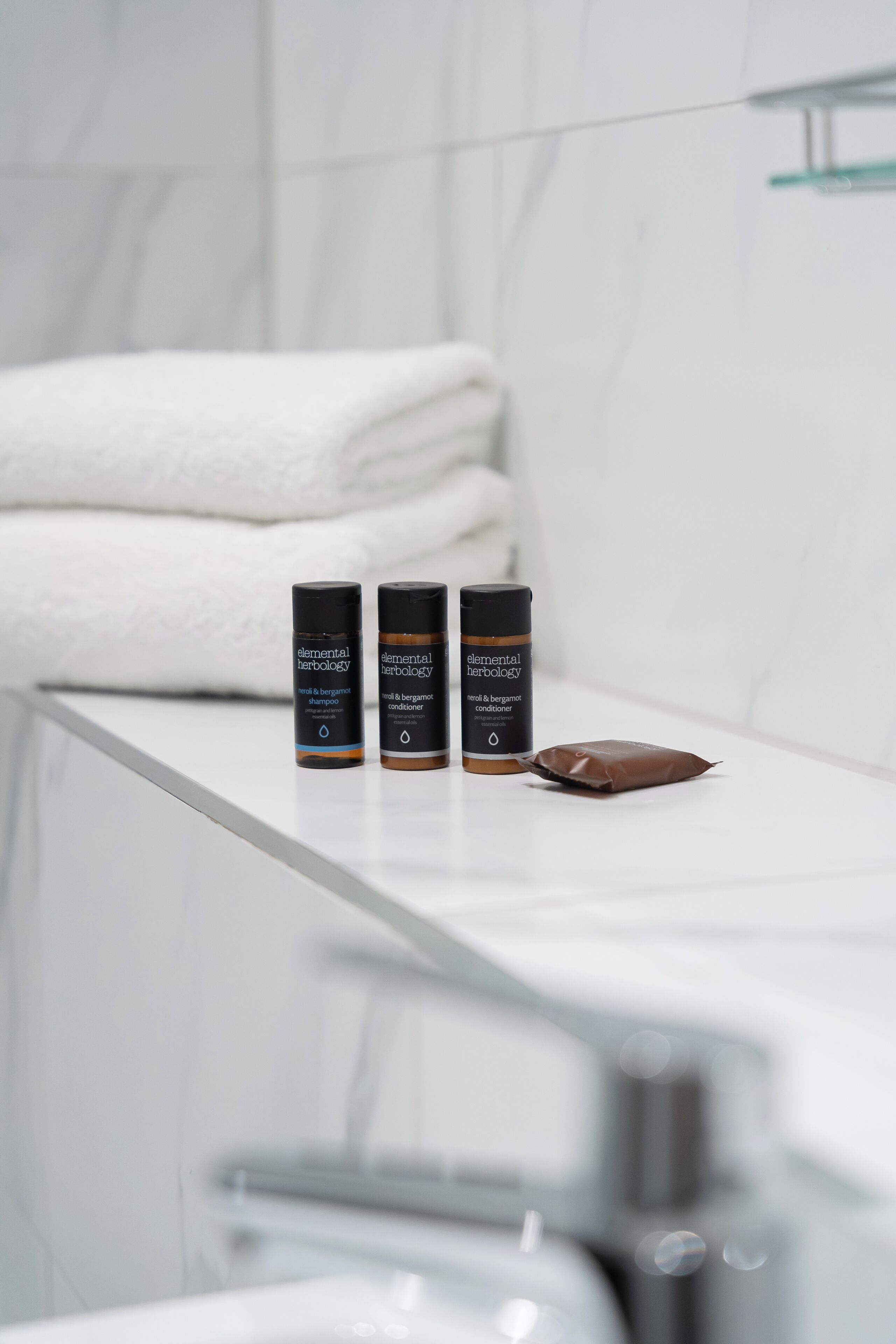 Ein Badezimmer mit einer weißen Marmorarbeitsplatte, zwei Flaschen mit Elemental Herbology Ha- und Bartprodukten und einer braunen Packung.
