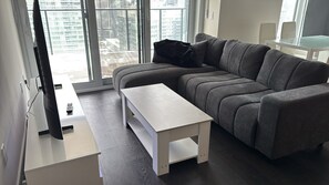 A modern living room with a grey sectional sofa, a white coffee table, and a large window offering a city view. - Luxury 2-bedroom 2 baths condo Downtown Toronto (Toronto)
