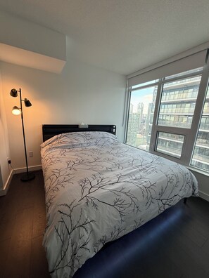 A bedroom with a bed, a floor lamp, and a window with a city view. - Luxury 2-bedroom 2 baths condo Downtown Toronto (Toronto)