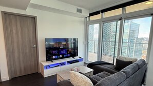 Ein modernes Wohnzimmer mit einem großen Flachbildfernseher, einem grauen Sofa und einem Fenster mit Blick auf die Stadt.