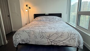 Ein Schlafzimmer mit einem großen Bett, einer Stehlampe und einem Fenster mit Blick auf die Stadt.