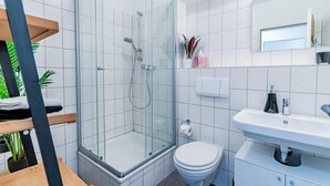 Une salle de bain moderne avec une douche à parois de verre, des toilettes blanches et un lavabo surmonté d’un miroir.