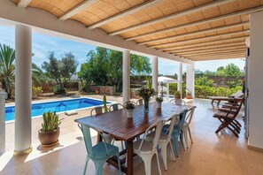 A covered patio with a pool, a wooden table, and chairs. - Amazing Location & Value! (Sant Josep de sa Talaia)