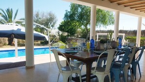 Ein Essbereich im Freien mit Pool, weißen Stühlen und einer überdachten Terrasse.