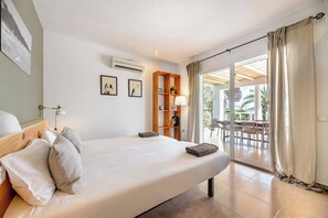 A bedroom with a bed, a wooden shelf, a lamp, and a view of an outdoor patio. - Amazing Location & Value! (Sant Josep de sa Talaia)