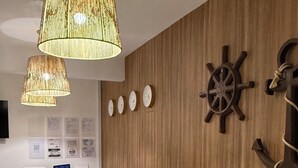 A reception area with a wooden wall, a desk, a white chair, and a decorative wall clock. - Pousada Mar da Vila (Cabo Frio)