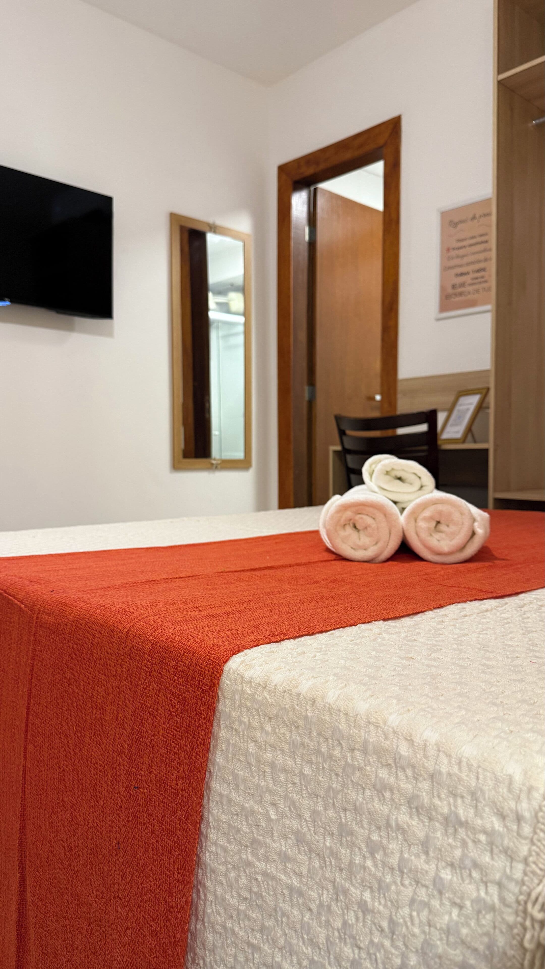 A hotel room with a bed, a television mounted on the wall, a wooden door, and a mirror.