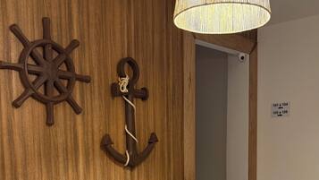 A modern room with two white chairs, a wooden wall with a ship's wheel and anchor decoration, and a hanging lamp.