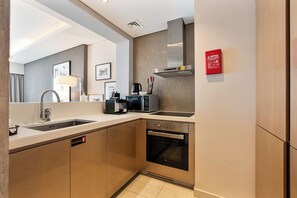 A modern kitchen with a sink, stove, and microwave. There is a fire blanket on the wall and a coffee machine. - Luxury 2 Bedroom | Near Burj Khalifa & Dubai Mall (Dubai)