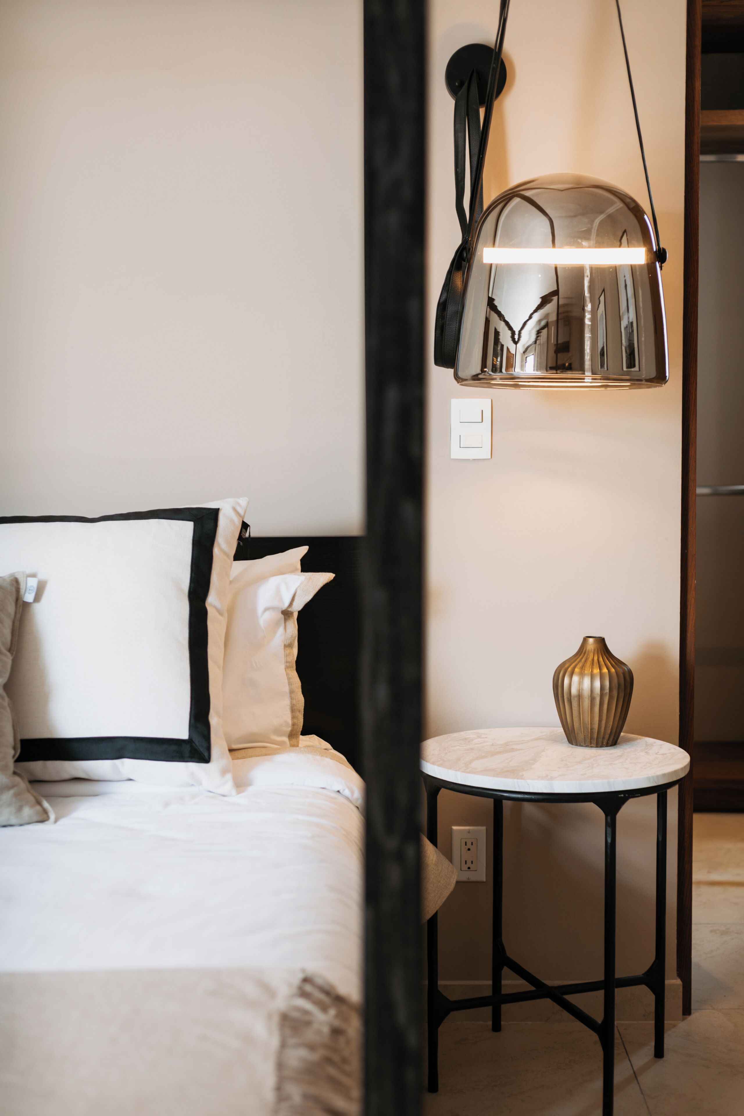 A hotel room with a bed, a bedside table with a lamp, and a small round table.