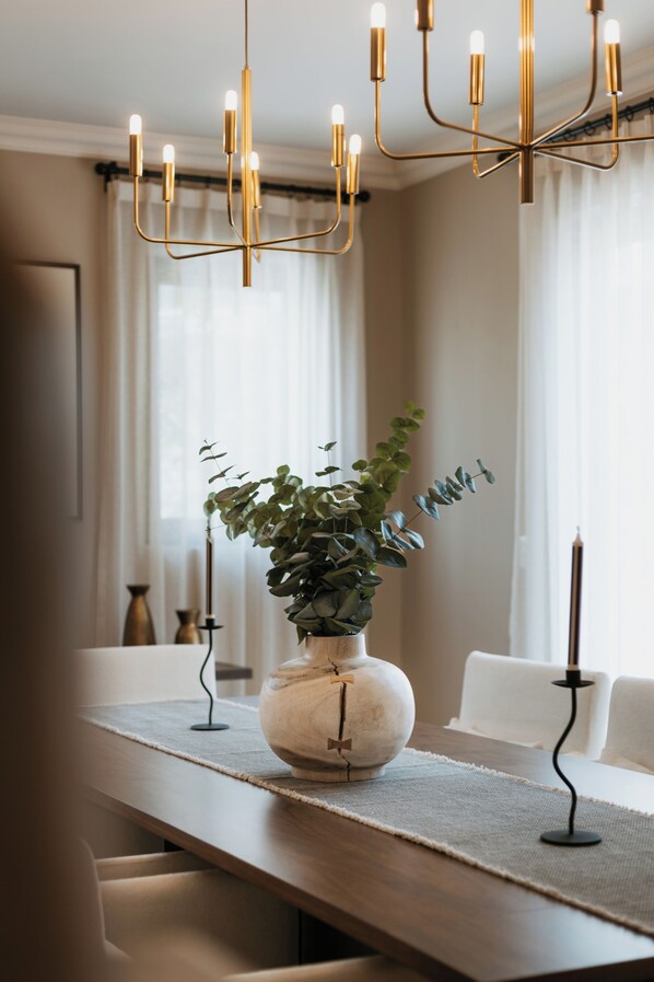 A dining table with a vase of green foliage, a candle, and a modern chandelier.