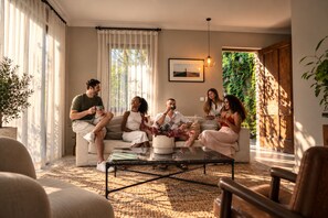 A group of people sitting on a sofa in a well-lit room with a large window, a framed picture on the wall, and a plant in the corner. - Trobbu Boutique Collection San Miguel de Allende - All Inclusive (San Miguel de Allende)