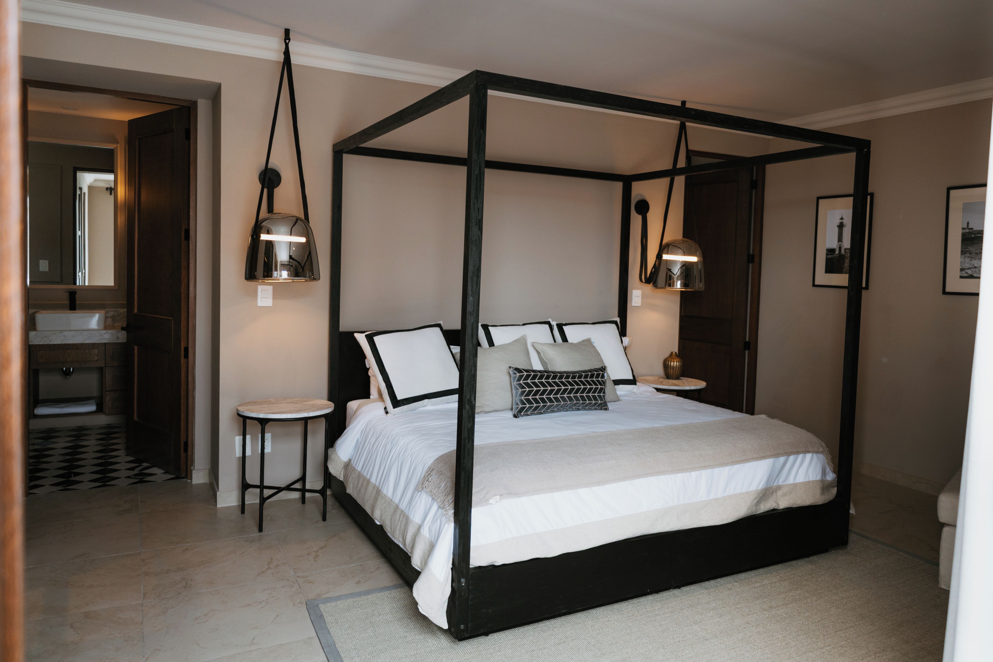 Un lit à baldaquin avec une couvre-lit noire et blanche, deux tables de chevet et deux lampes fixées au mur.