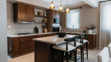 Cocina con armarios de madera, una isla central con taburetes, estufa a gas e iluminación colgante.