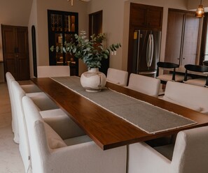 A dining area with a long wooden table, white upholstered chairs, a vase with green foliage, and wooden cabinets. - Trobbu Boutique Collection San Miguel de Allende - All Inclusive (San Miguel de Allende)