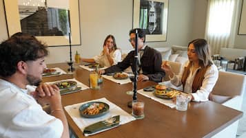 A group of people seated around a wooden table in a well-lit room with a modern interior design, featuring framed artwork on the walls.
