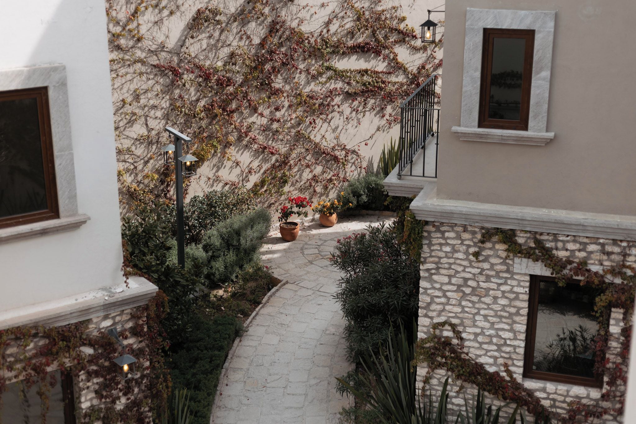 A narrow stone pathway flanked by lush greenery and flowering plants, leading to a staircase.