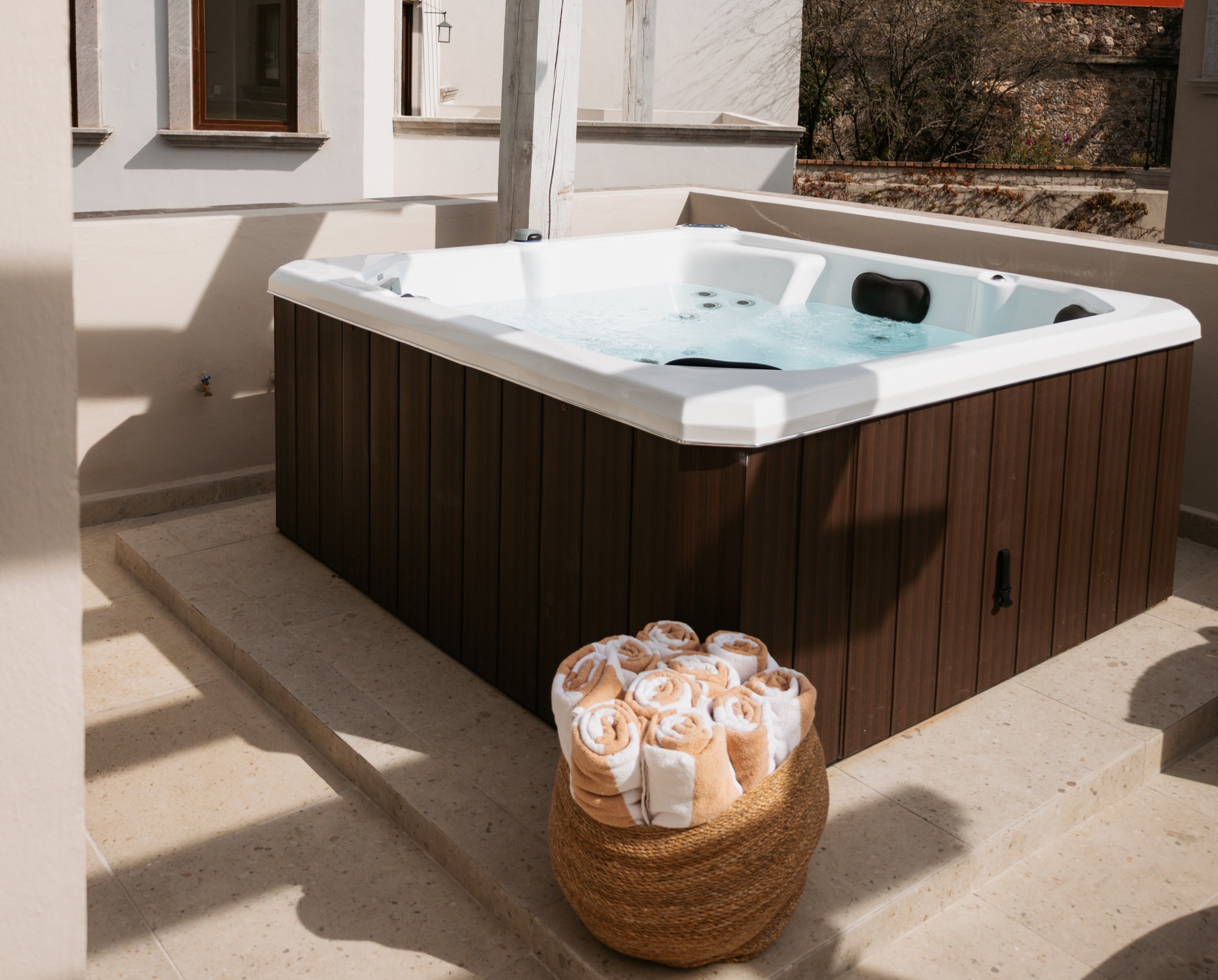 Un jacuzzi con revestimiento de madera, una cesta de toallas y una pared de piedra al fondo.