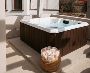 Un bain à remous avec un revêtement extérieur en bois, un panier rempli de serviettes et un mur de pierres en arrière-plan.