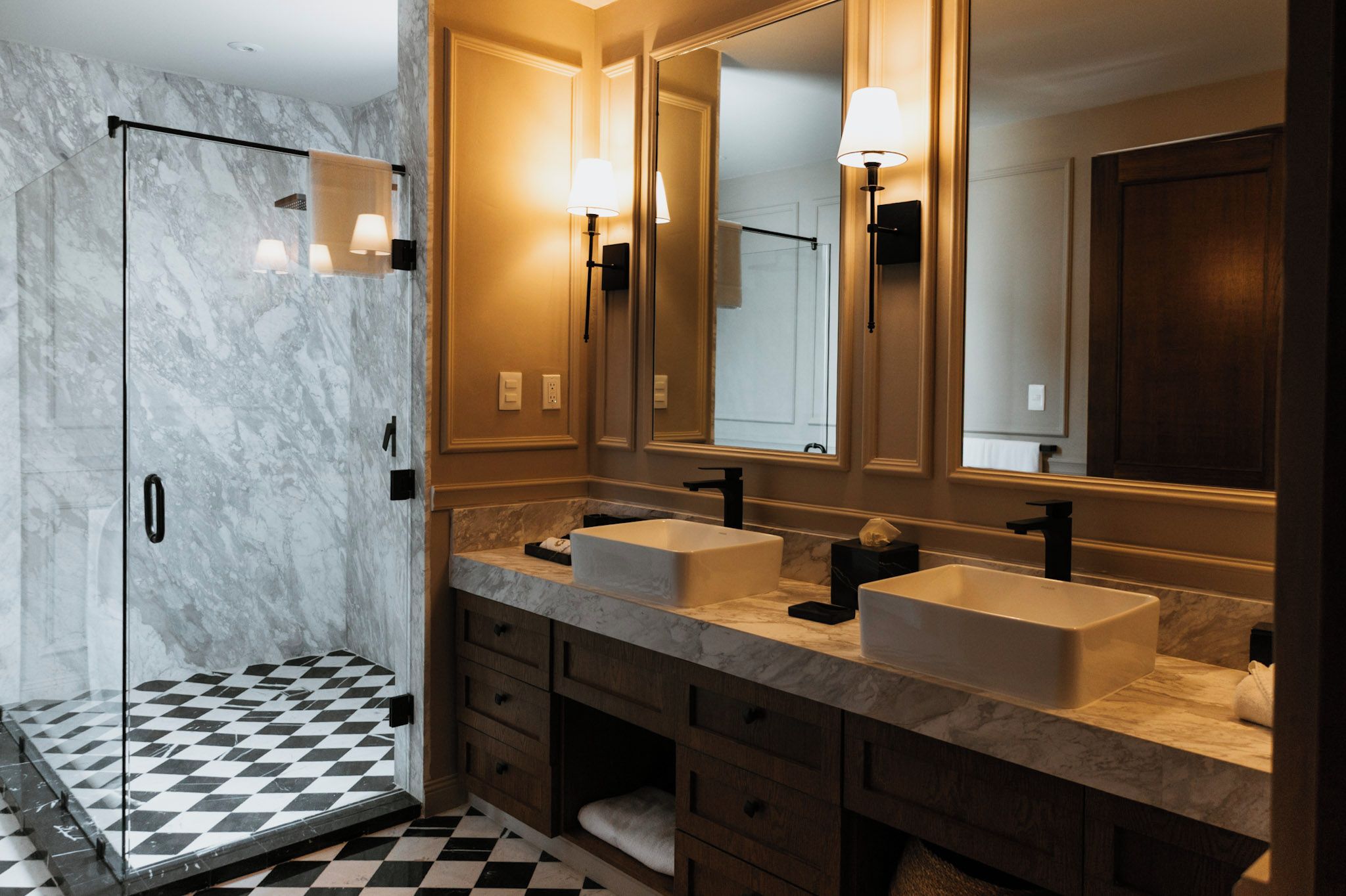 Un baño moderno con dos lavamanos, ducha y piso de cuadros.