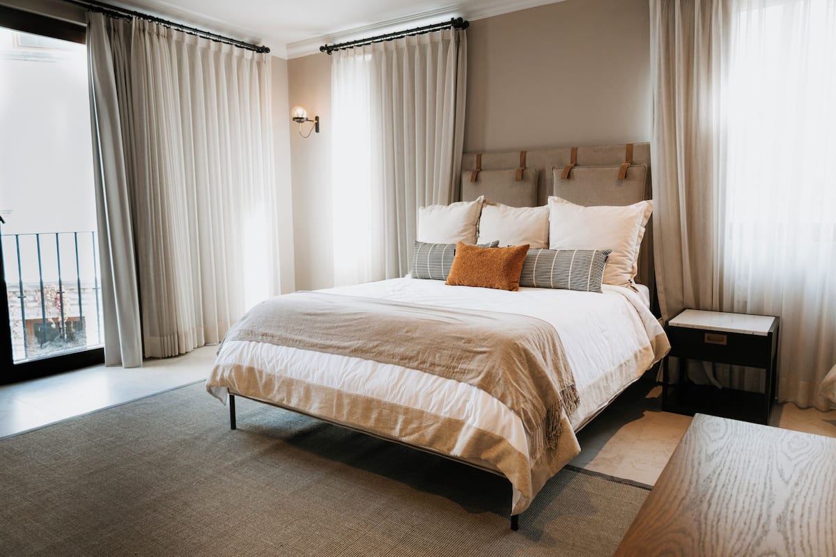 A modern bedroom with a large bed, a bedside table, and a view of the outdoors.