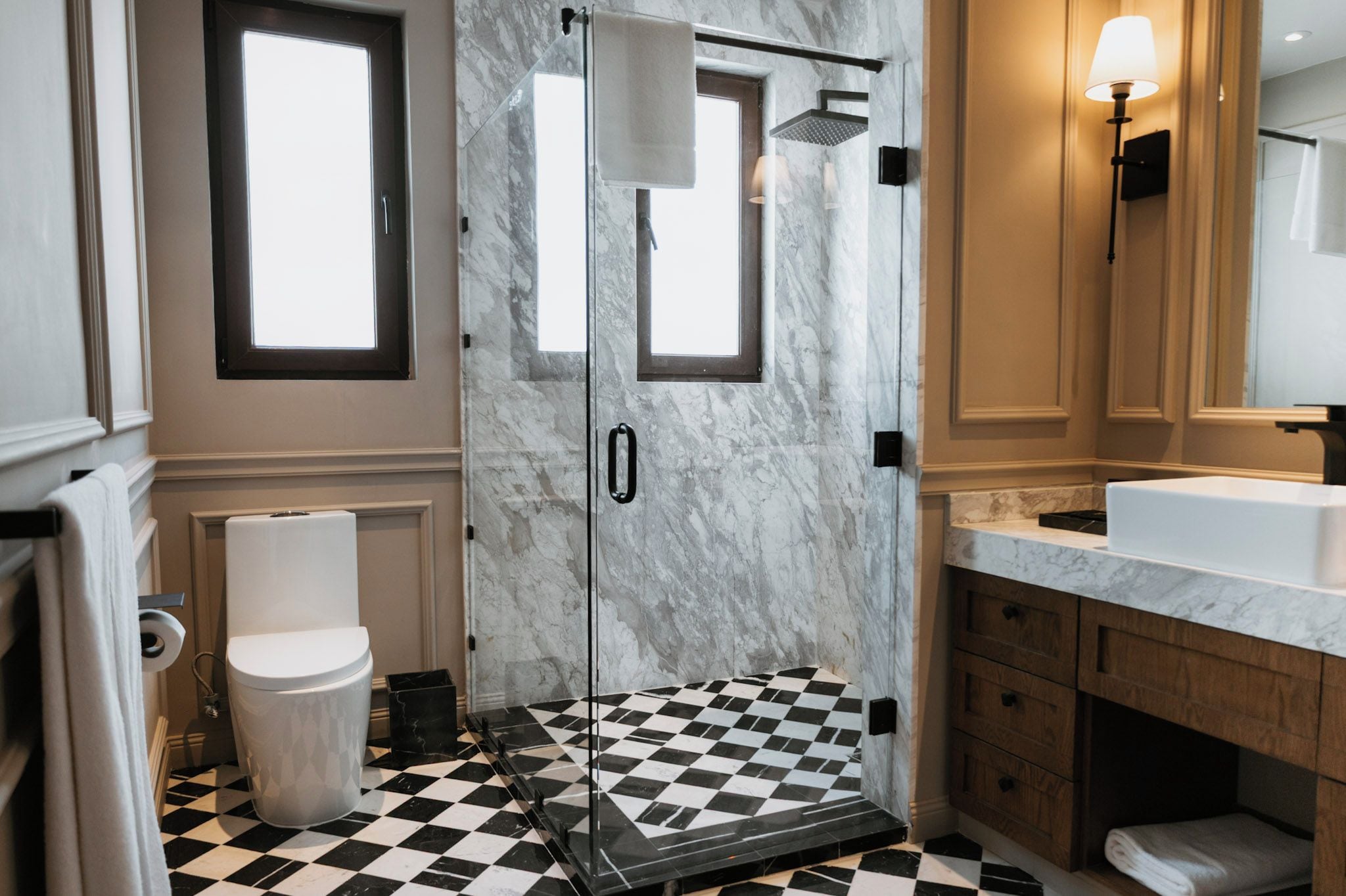 A bathroom with a checkered floor, a white toilet, a shower with a glass door, and a vanity with a mirror.