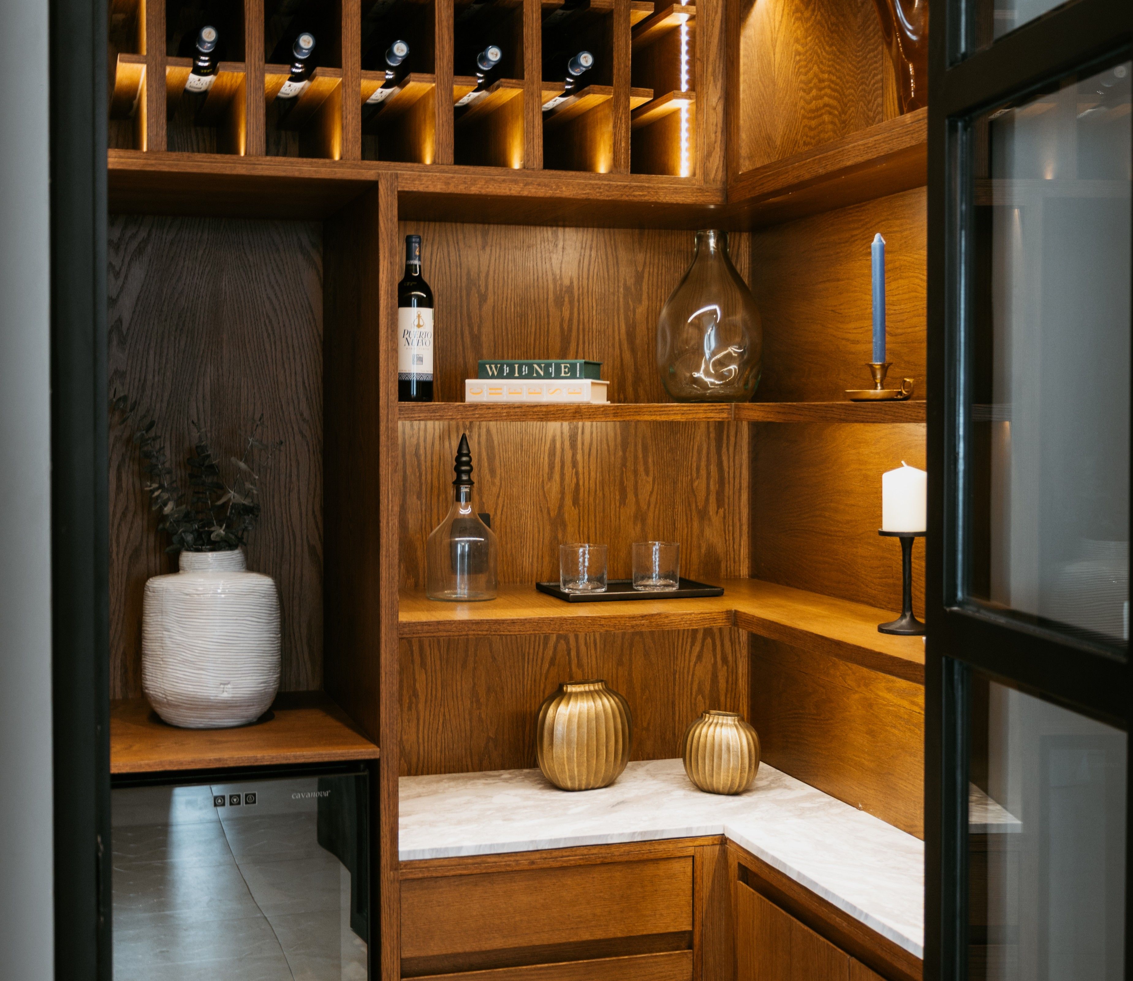 Un porte-bouteilles en bois contenant des bouteilles de vin, une bouteille de vin, un verre et une bougie, le tout posé sur une étagère.