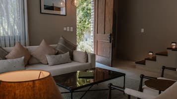 A modern living room with a sofa, coffee table, and chairs. There is a window with curtains, a picture on the wall, and a door leading outside.