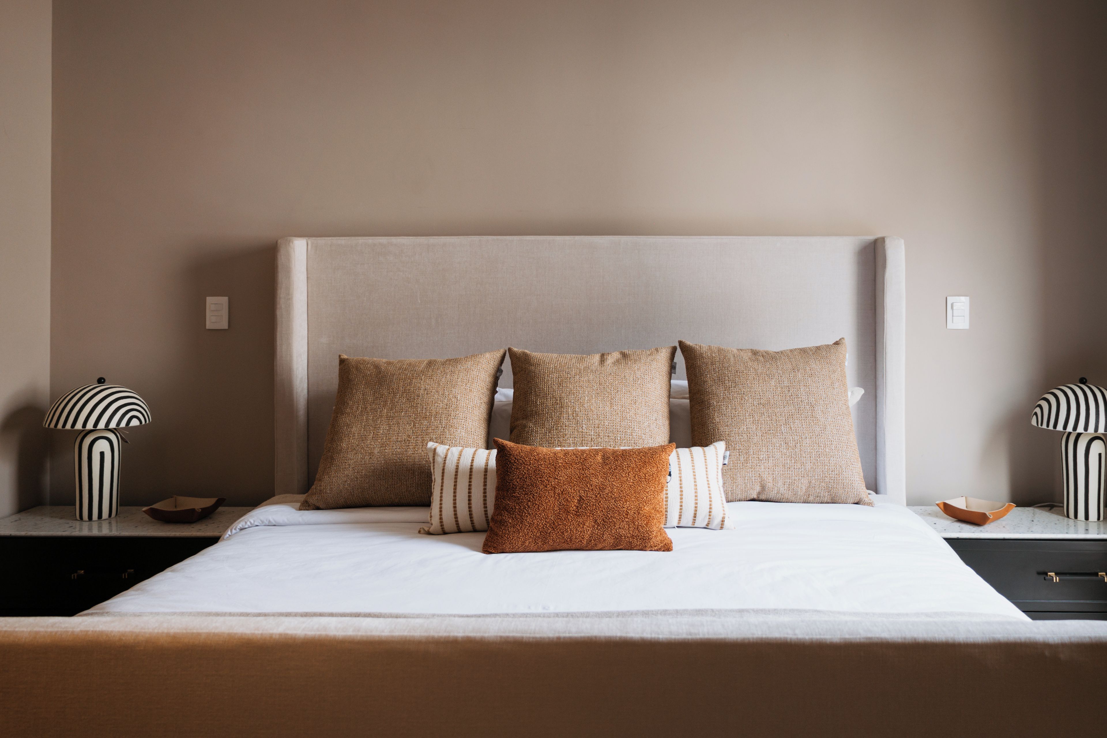 A bed with a headboard, multiple pillows, and two bedside tables with lamps.