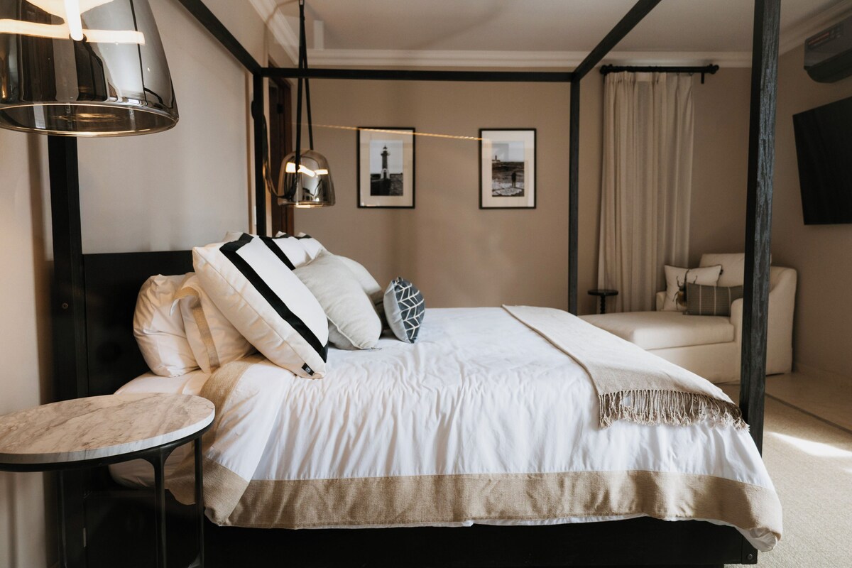 Un dormitorio ordenado con una cama grande, una mesita de noche, un sofá y un televisor montado en la pared.