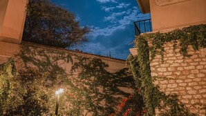 A night scene with a moonlit sky, a stone wall with climbing plants, and a building with a balcony. - Trobbu Boutique Collection San Miguel de Allende - All Inclusive (San Miguel de Allende)